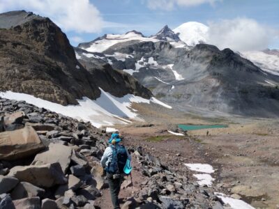 The trail just below Panhandle Gap Hiker near Panhandle Gap with view of Mt Rainier on the Wonderland Trail.